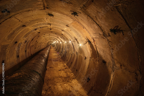 Long underground round concrete tunnel with a pipe, lit by incandescent lamps. Underground tunnel of a heating main or a water supply system. photo