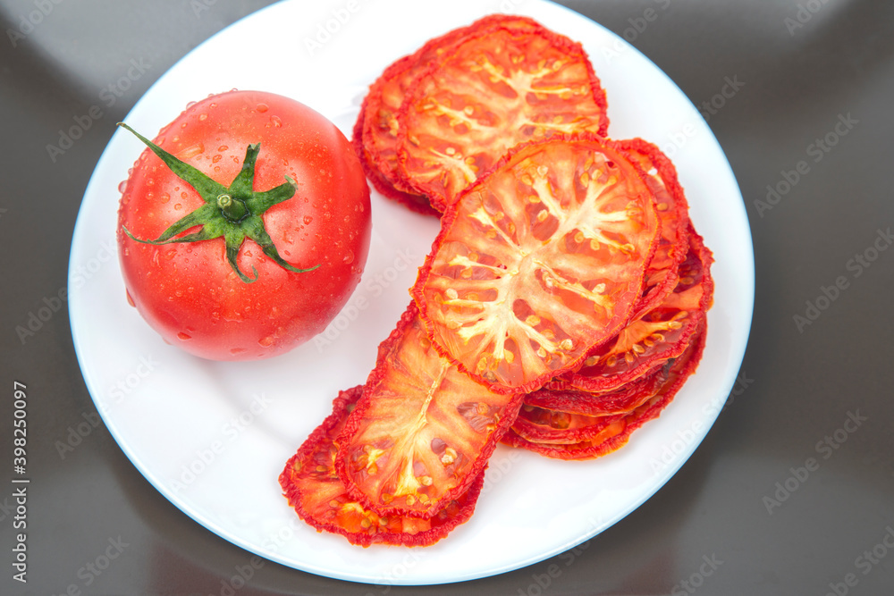 Fresh red tomato and dried tomato slices on a plate. Vitamin vegetable food