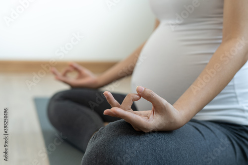Pregnant mother is doing yoga at home for good health. Pregnant women exercise and practice meditation for relaxation. Pregnancy yoga and fitness concept.