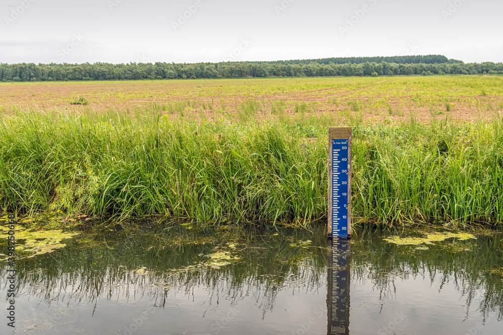 Blue water level scale with white markings in the water of a ditch. In the Netherlands the water level is measured in meters above or below the Amsterdam Ordnance Datum or Normal Amsterdams Peil (NAP)