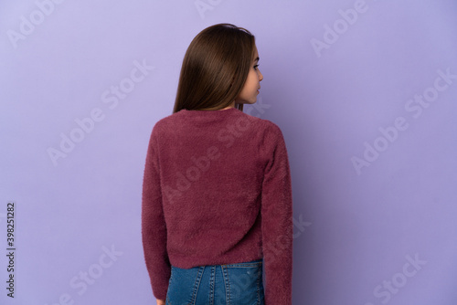Little girl isolated on purple background in back position and looking side