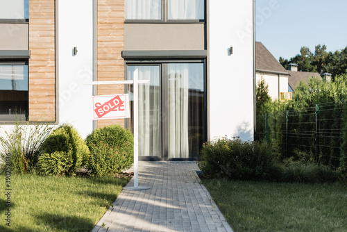 Front facade of modern house near lawn and sign with sold lettering © LIGHTFIELD STUDIOS