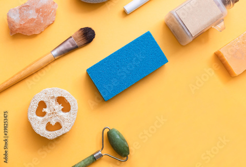 Beauty product for home spa treatment with copy space. Jade roller, loofah, pumice stone, solid shampoo, bath salt and wooden brush on yellow background, flat lay.