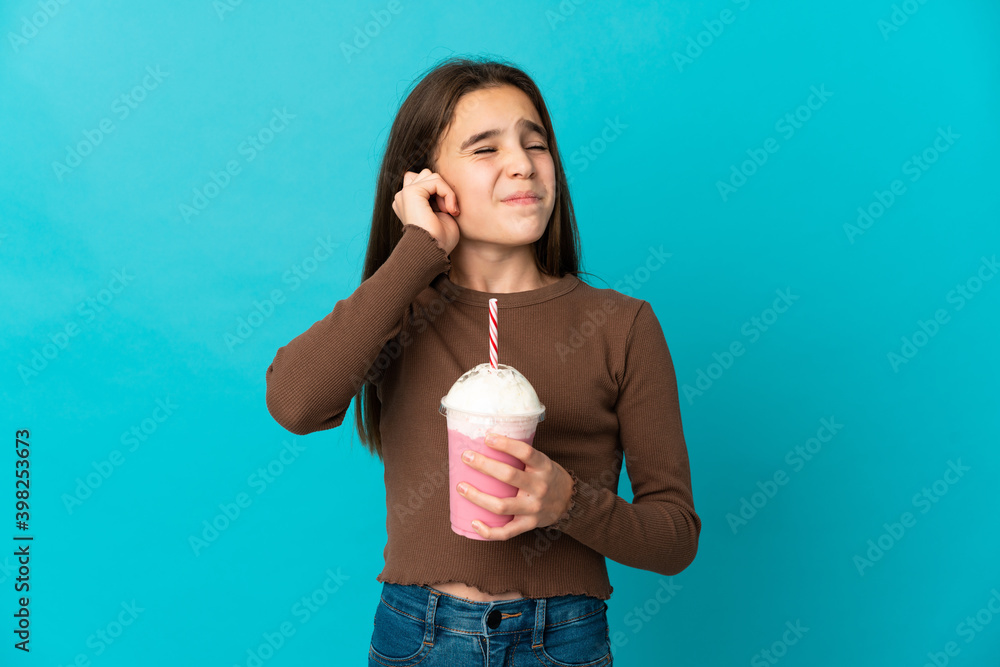 Little girl with strawberry milkshake isolated on blue background frustrated and covering ears Little girl with strawberry milkshake isolated on blue background frustrated and covering ears