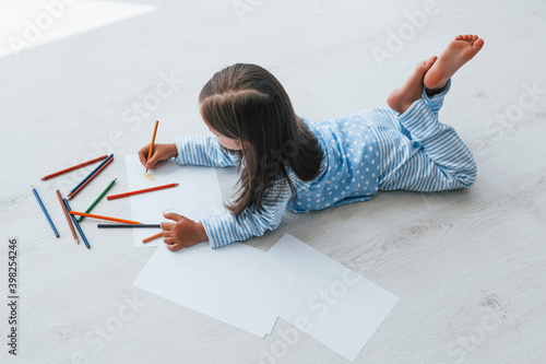 Lying on the floor and drawing. Cute little girl indoors at home alone
