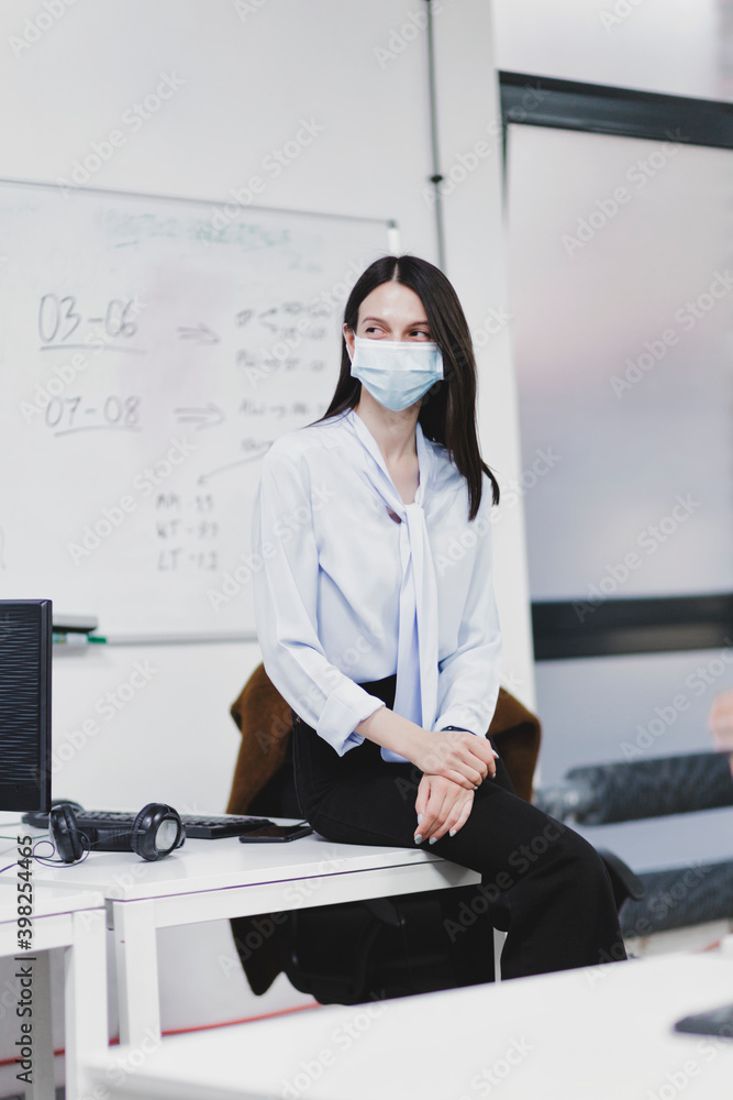 Woman in face mask sitting on desk in office