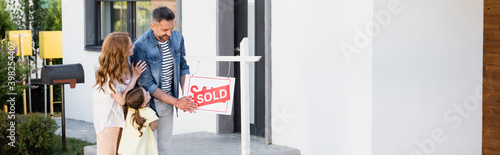 Fotografie Positive father holding sign with sold lettering near wife and daughter, banner
