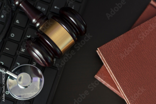 Top view of Judge's gavel and medical stethoscope on computer keyboard and books on woodeb table