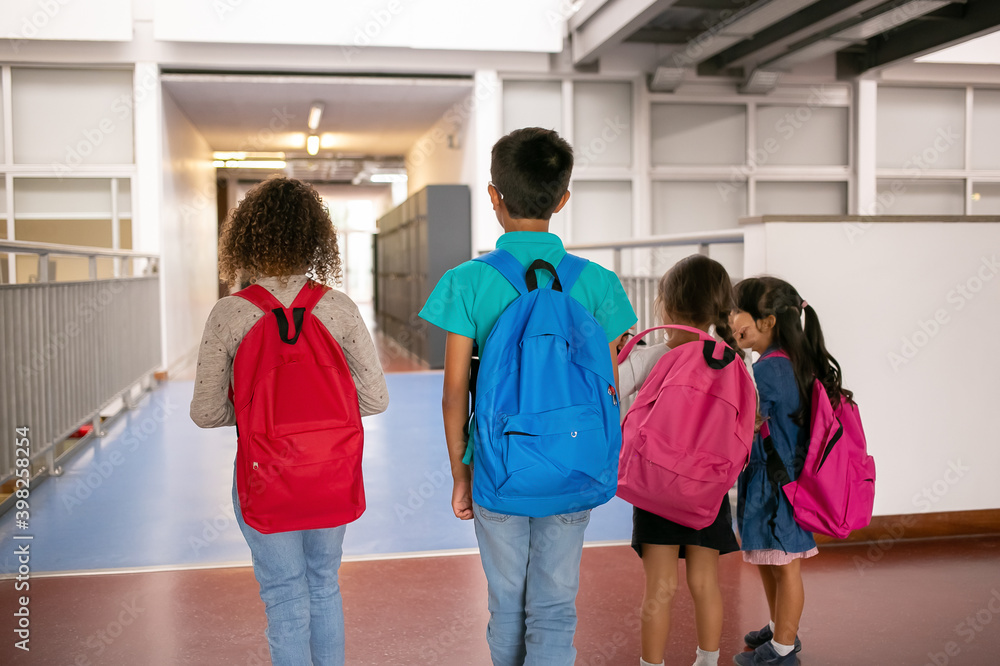 Group of schoolkids with colorful backpacks walking and standing in school corridor. Back view, full length. Education or back to school concept