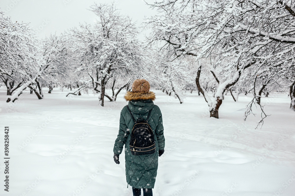 Woman in winter clothes with backpack walking in the woods in winter.  Snow falling, white winter background 