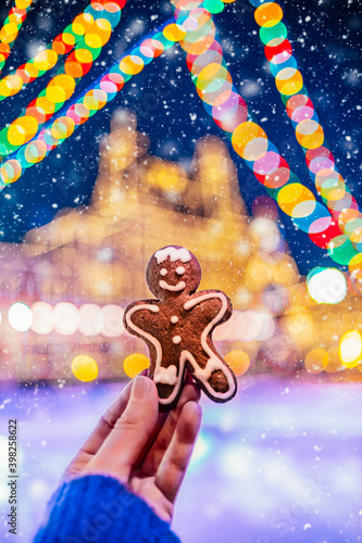 Gingerbread man cookie on the blurred Christmas lights background.  Woman's hand holding gingerbread man. New Year and winter holidays background.   © oluuuka