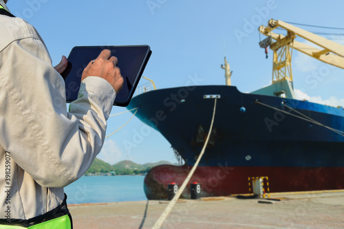 Workers in shipyard hand holding tablet check condition for ship repair by front ship in shipyard background