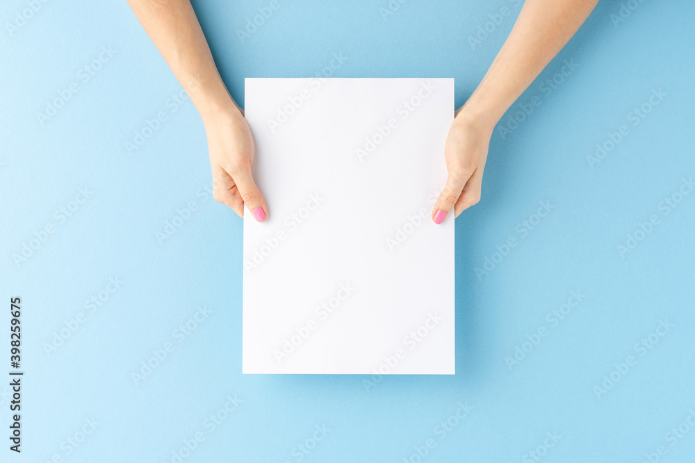 Female hands showing empty paper sheet on blue background. Close up Female hands showing empty paper sheet on blue background. Close up