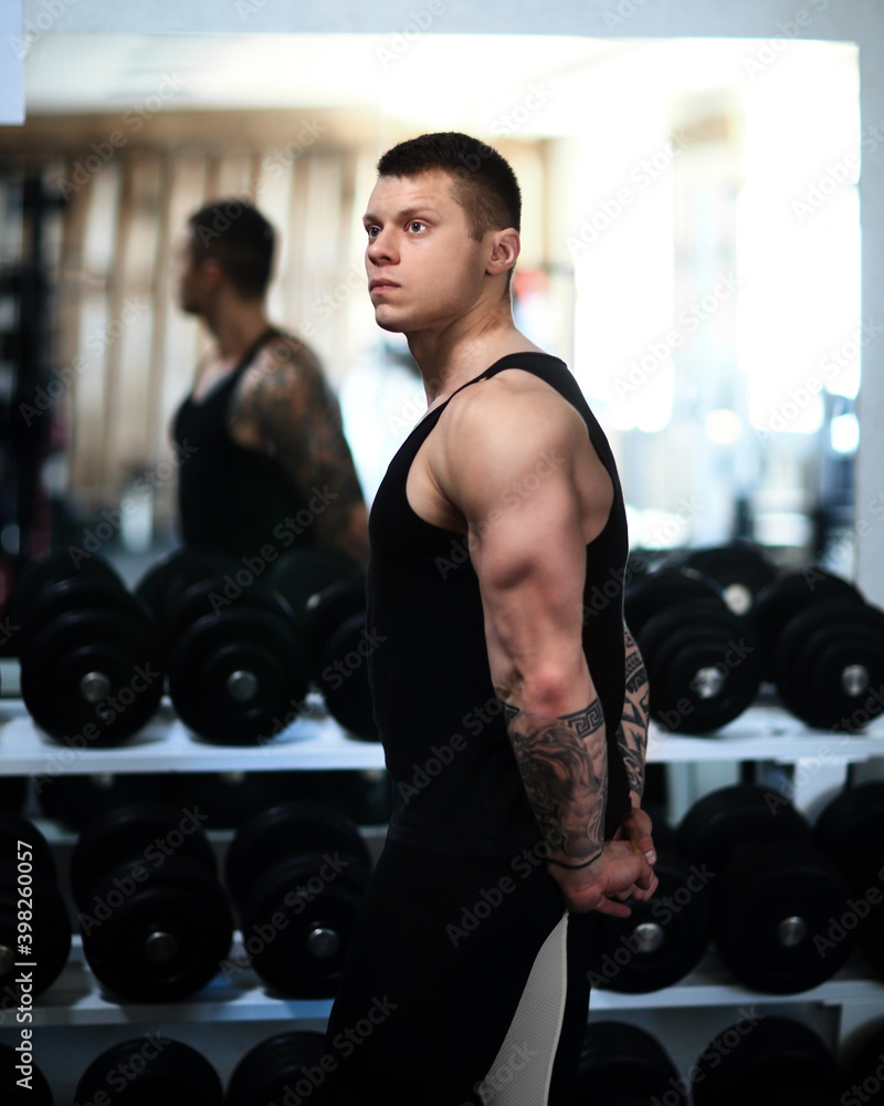 young bodybuilder standing next to the mirror in the gym. young bodybuilder standing next to the mirror in the gym.
