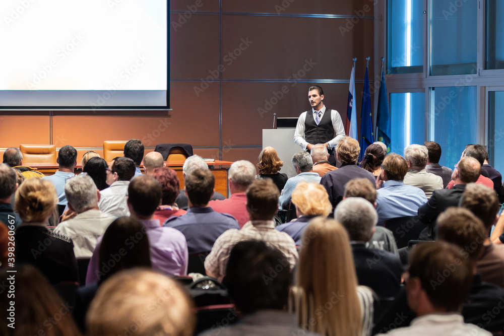 Speaker giving a talk in conference hall at business meeting event. Rear view of unrecognizable people in audience at the conference hall. Business and entrepreneurship concept. Speaker giving a talk in conference hall at business meeting event. Rear view of unrecognizable people in audience at the conference hall. Business and entrepreneurship concept.