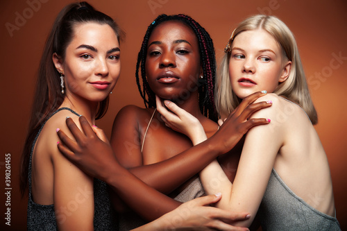 young pretty asian, caucasian, afro woman posing cheerful together on brown background, lifestyle diverse nationality people concept