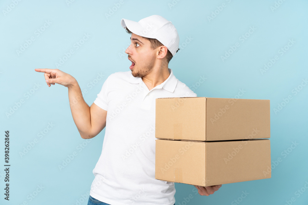 Delivery caucasian man isolated on blue background pointing finger to the side Delivery caucasian man isolated on blue background pointing finger to the side