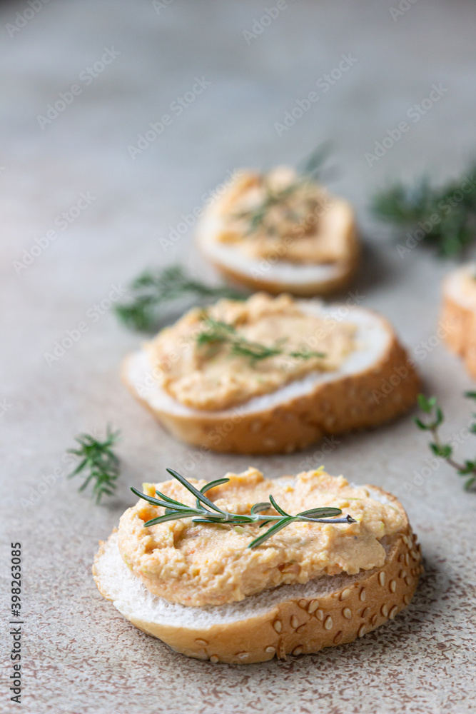 Homemade pate, spread or mousse in glass jar with sliced bread and herbs, light concrete background.