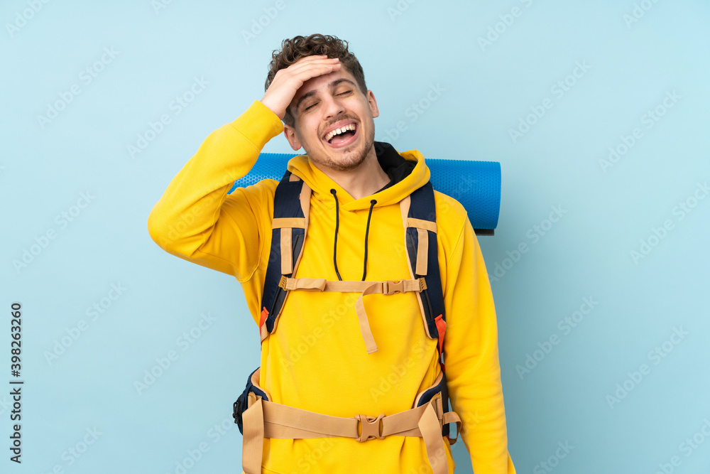 Young mountaineer man with a big backpack isolated on blue background laughing Young mountaineer man with a big backpack isolated on blue background laughing