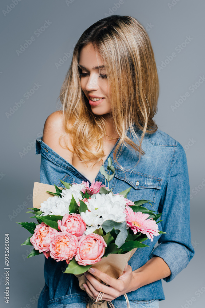 seductive woman in denim shirt holding bouquet while posing with naked shoulder isolated on grey seductive woman in denim shirt holding bouquet while posing with naked shoulder isolated on grey