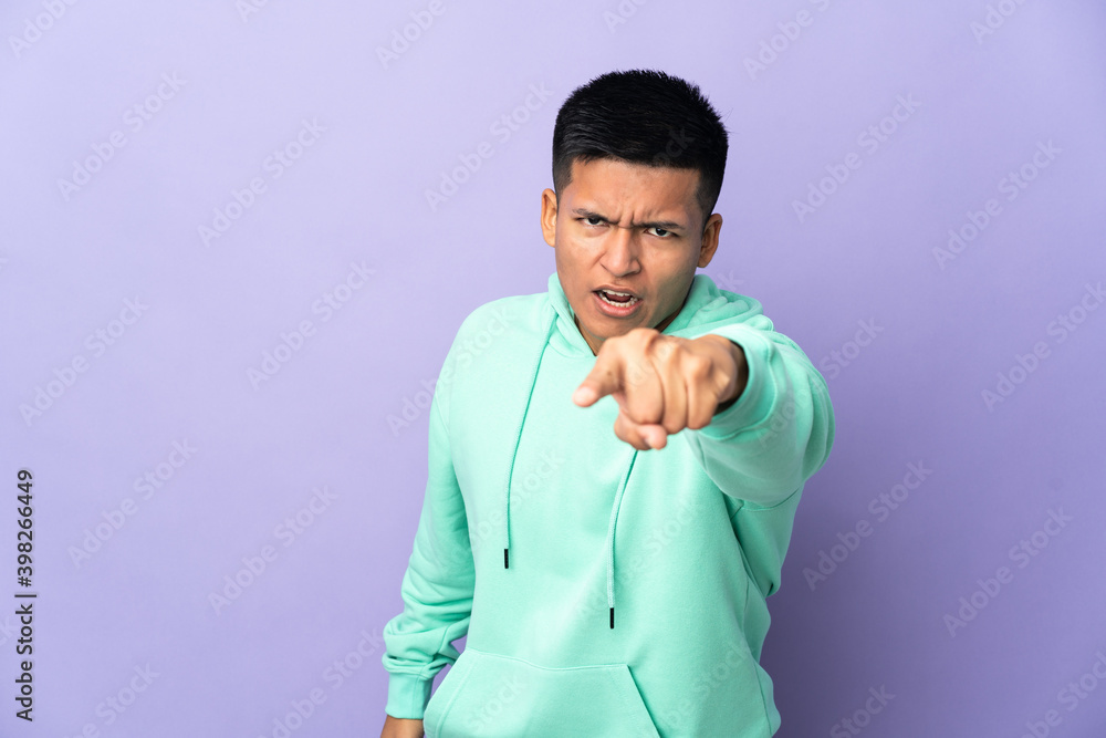 Young Ecuadorian man isolated on purple background frustrated and pointing to the front Young Ecuadorian man isolated on purple background frustrated and pointing to the front