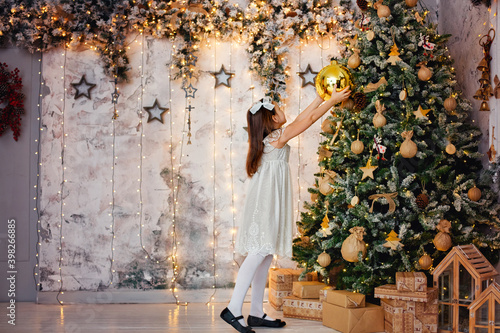 A big Golden Christmas ball in the hands of a girl. On the background of a garland of lights and a decorated Christmas tree. Festive mood. Hangs a balloon on the Christmas tree.