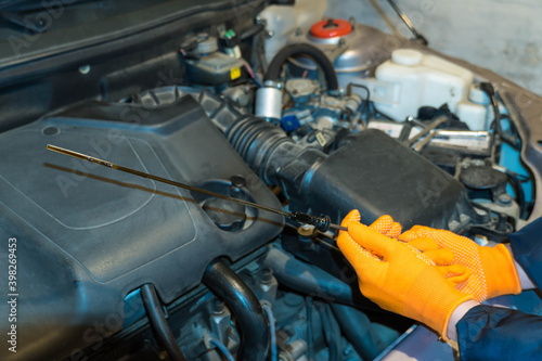Image of hands in orange gloves above the car engine, holding the oil level indicator in the car engine.