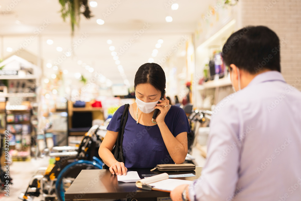 Woman in protective mask talking on cell phone cashier counter.