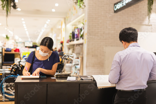 Woman in protective mask signing documents at cashier counter in shopping mall.