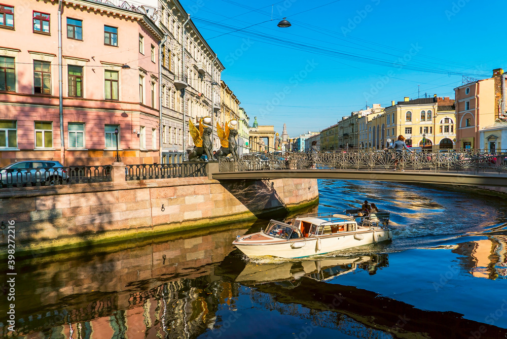 Tourist boat sails under the Bank bridge with griffins on the Griboyedov canal. Saint-Petersburg.