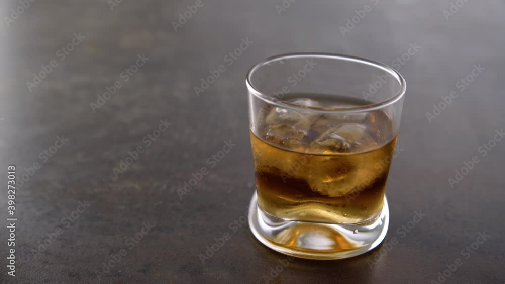 Man drinking glass of aged golden whiskey with ice cubes and putting it on the table. Hand putting amber colored alcohol beverage with rocks on rock background Man drinking glass of aged golden whiskey with ice cubes and putting it on the table. Hand putting amber colored alcohol beverage with rocks on rock background