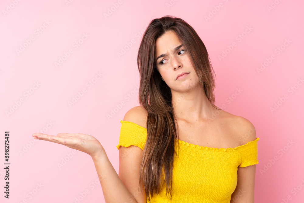 Teenager Brazilian girl over isolated pink background holding copyspace with doubts Teenager Brazilian girl over isolated pink background holding copyspace with doubts