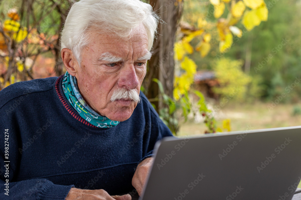 Old man working on laptop in his garden. A senior thoughtful man staring on the screen and making notes. Old man working on laptop in his garden. A senior thoughtful man staring on the screen and making notes.