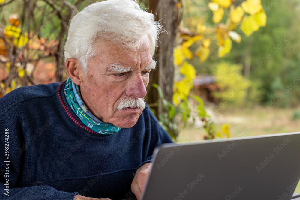 Old man working on laptop in his garden. A senior thoughtful man staring on the screen and making notes. Old man working on laptop in his garden. A senior thoughtful man staring on the screen and making notes.
