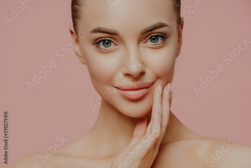 Fotografie Cropped shot of attractive calm woman touches face gently, has direct gaze at ca