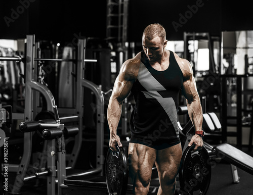 Muscular athletic bodybuilder fitness model doing exercises in gym.