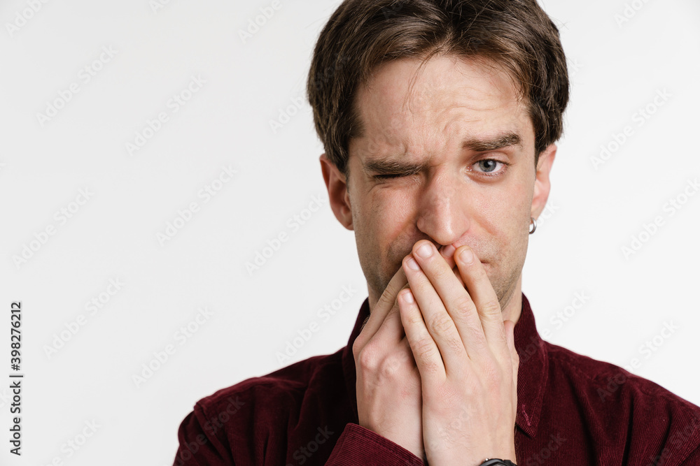 Handsome confused young man covering his mouth and winking Handsome confused young man covering his mouth and winking