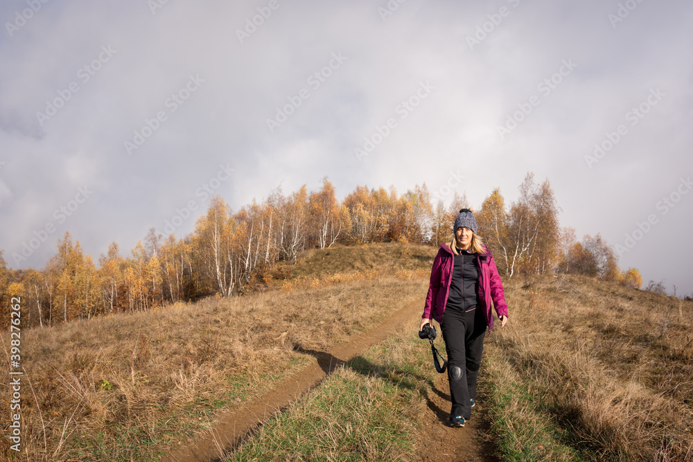 Adult woman hiking in the hills photographing trees with yellow leaves Adult woman hiking in the hills photographing trees with yellow leaves