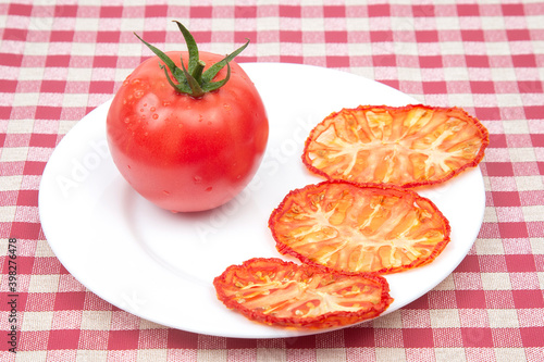 Fresh red tomato and dried tomato slices on a plate. Vitamin vegetable food