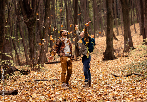 Two young hikers with backpack walking in forest and throwing leaves in the air.