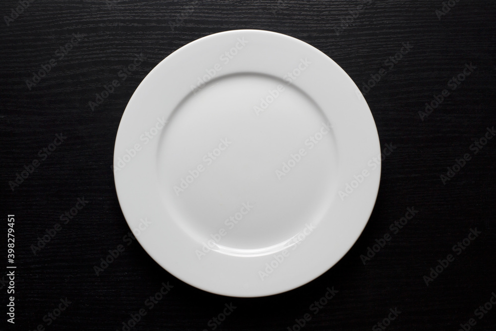 Round, white, empty plate on a black wooden background. Round, white, empty plate on a black wooden background.