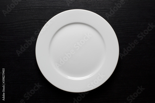 Round, white, empty plate on a black wooden background.