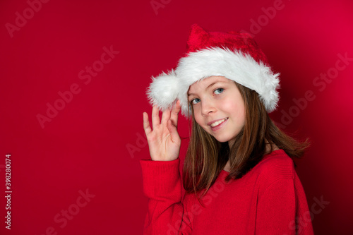 pretty young girl with Santa Claus cap and red pullover in front of red background