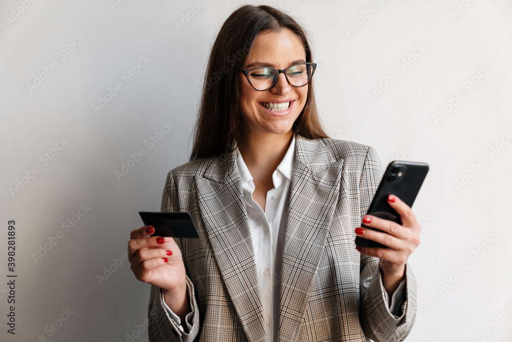 Beautiful joyful businesswoman posing with credit card and cellphone Beautiful joyful businesswoman posing with credit card and cellphone