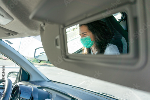 A shot of a woman with protective face-mask focused through the passenger mirror of the car