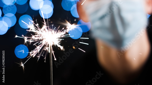 Close up of man with face mask holding sparkler for christmas and new year party. Celebrating at coronavirus lockdown.