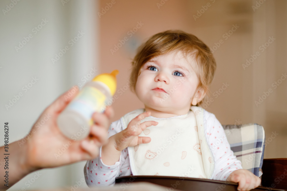 Adorable baby girl drinking formula milk from bottle. food, child, feeding and people concept -cute toddler, daughter with spoon sitting in highchair and eating at home. Adorable baby girl drinking formula milk from bottle. food, child, feeding and people concept -cute toddler, daughter with spoon sitting in highchair and eating at home.