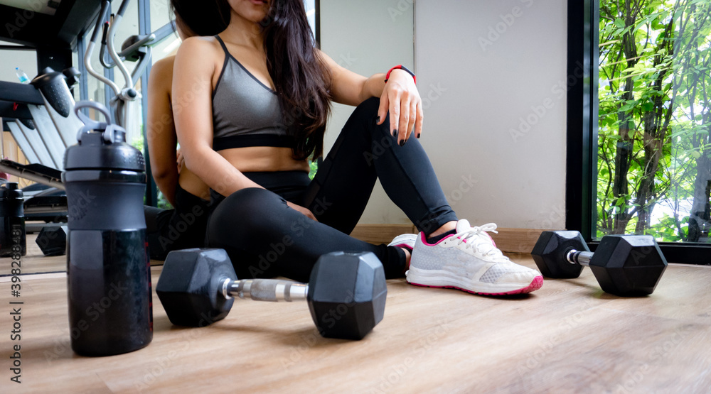 Obraz premium Woman exercise workout in gym fitness breaking relax after training sport with dumbbell and water bottle.