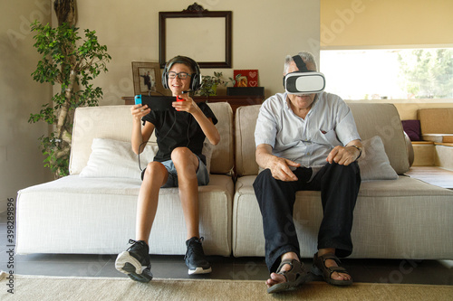 Nonno e nipote giocano con giochi elettronici seduti nel divano del salotto photo