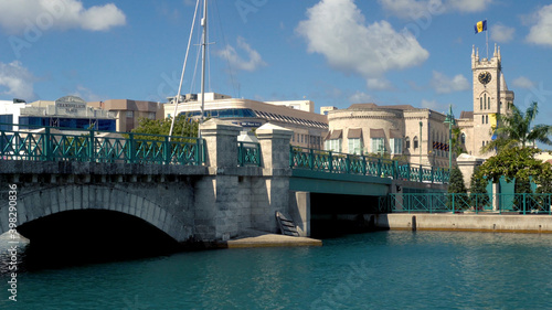 Bridgetown, Barbados: Chamberlain bridge with people passing and Parliament building with the flag on top of the tower in the background photo